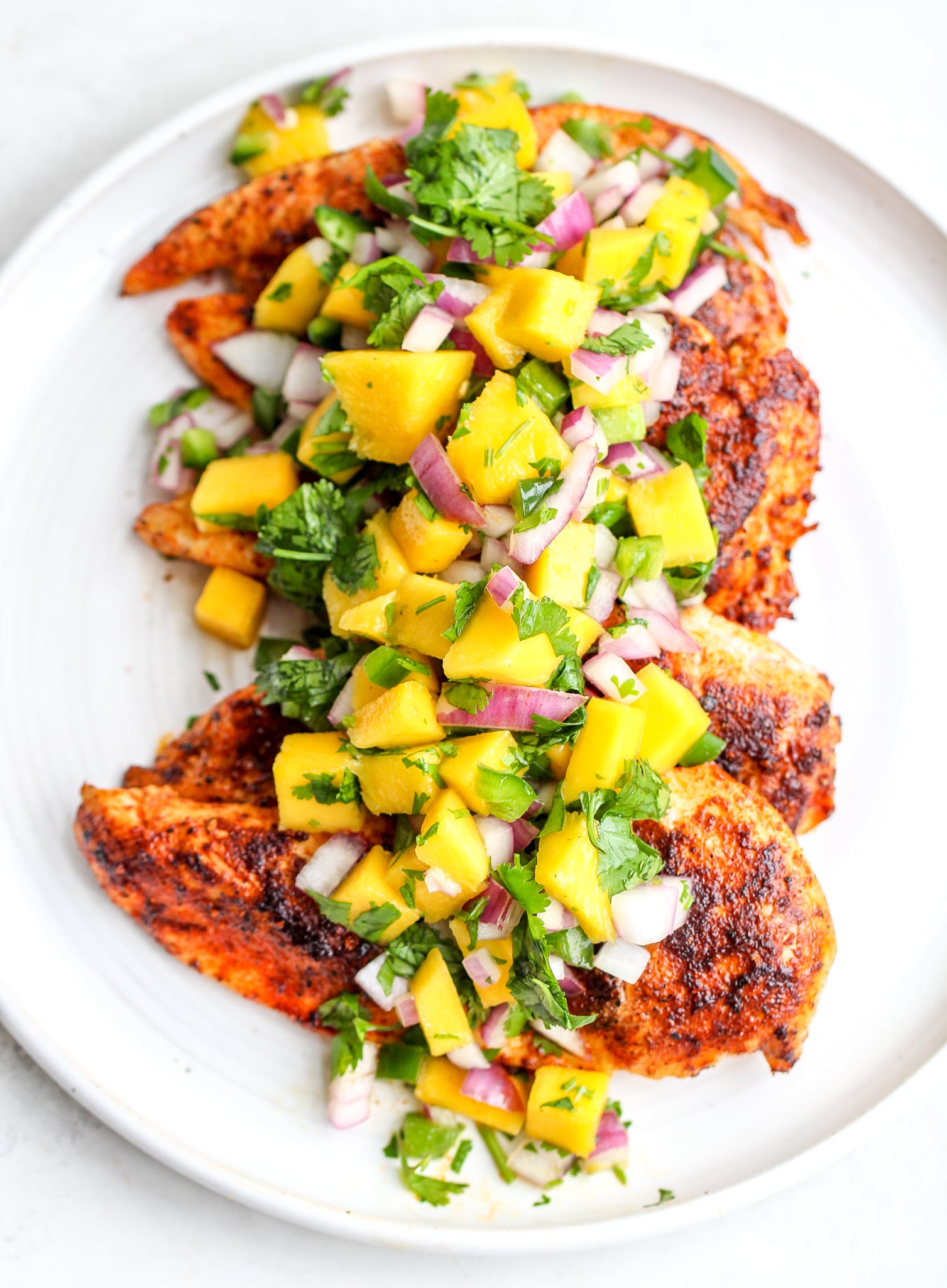 fresh mango salsa spread over cooked spiced chicken breast on a white serving platter
