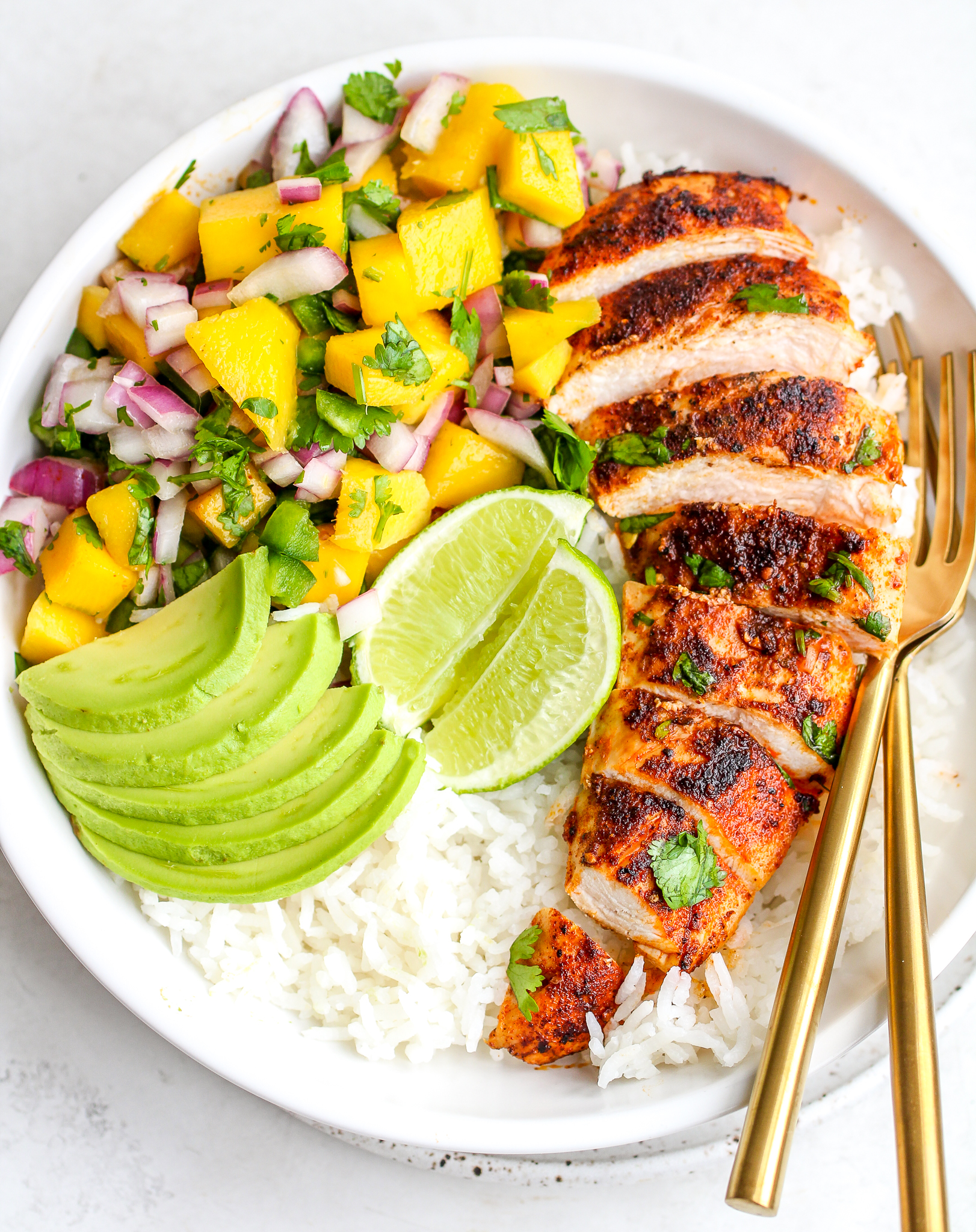 sliced spiced chicken breast over cooked white rice with fresh mango salsa on the side - as well as sliced avocado and lime wedges 