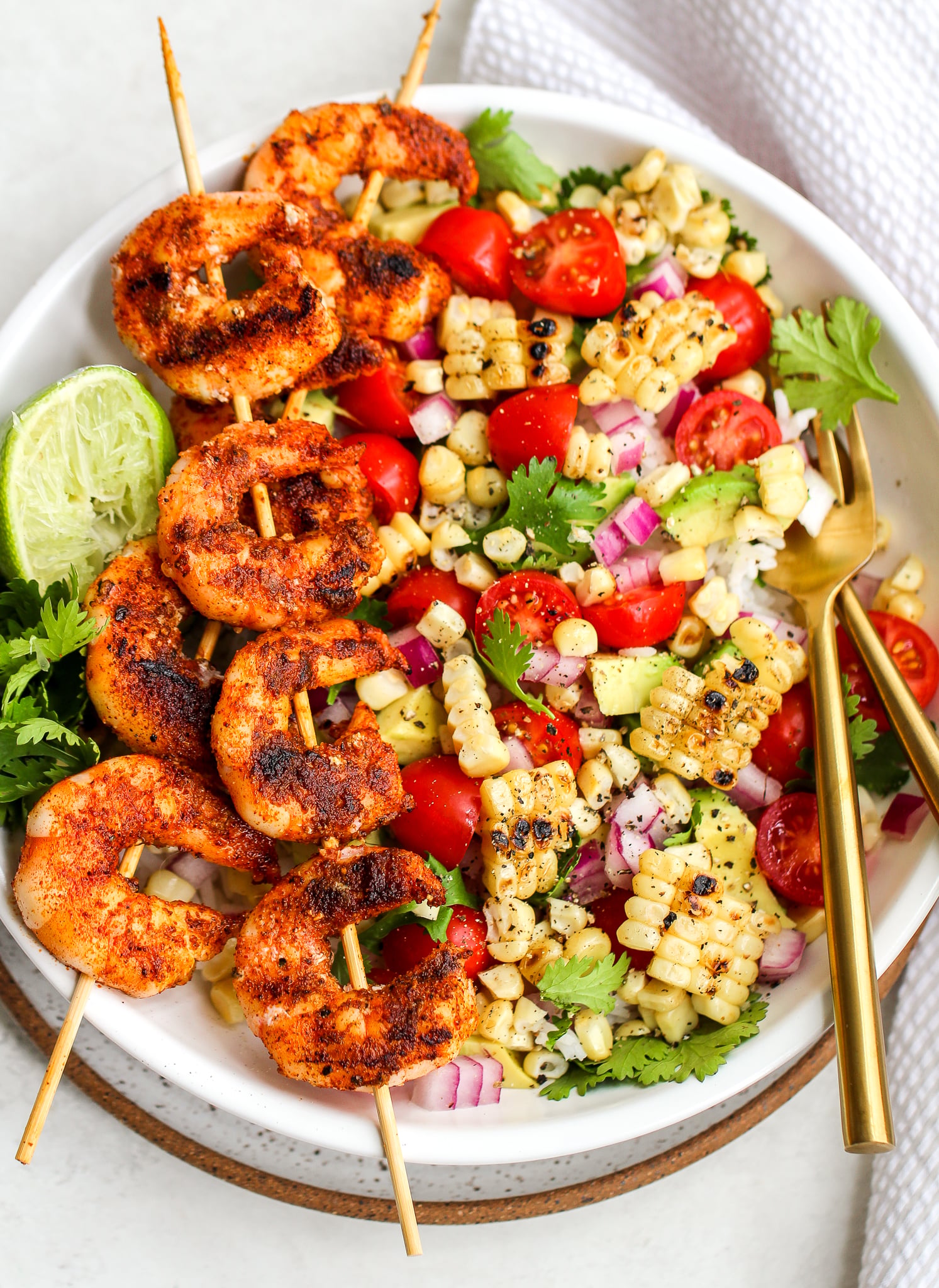 spiced grilled shrimp on skewers over a bowl of rice and fresh salsa ingredients 