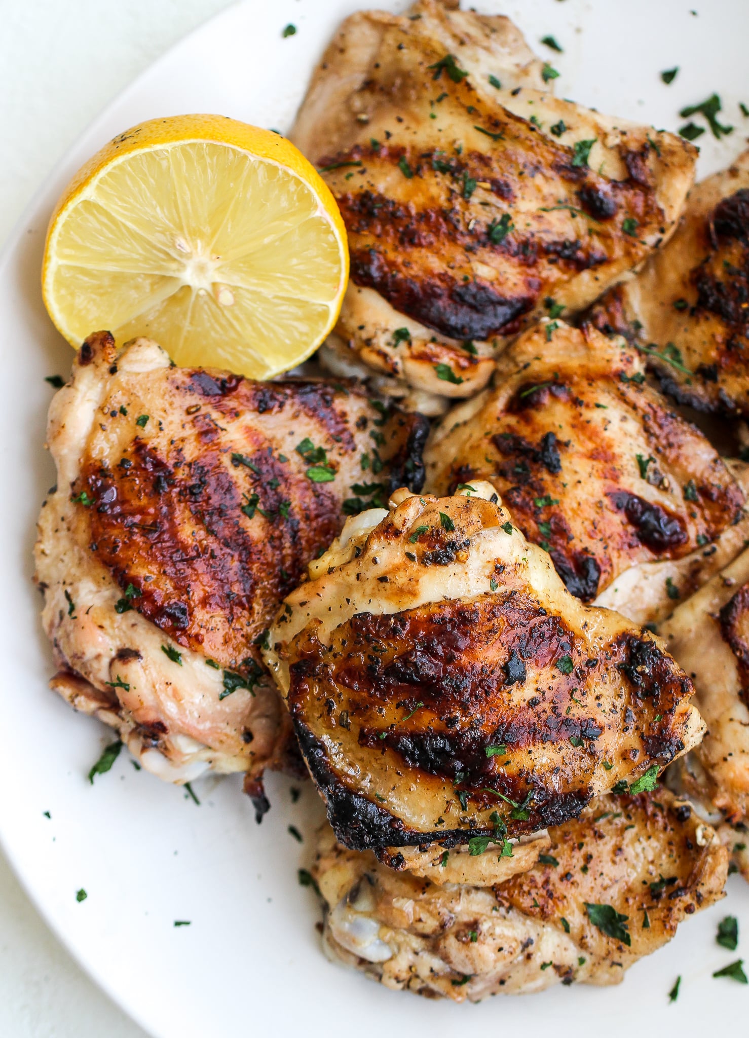 platter of grilled italian marinated chicken thighs with parsley on top and lemon on the side
