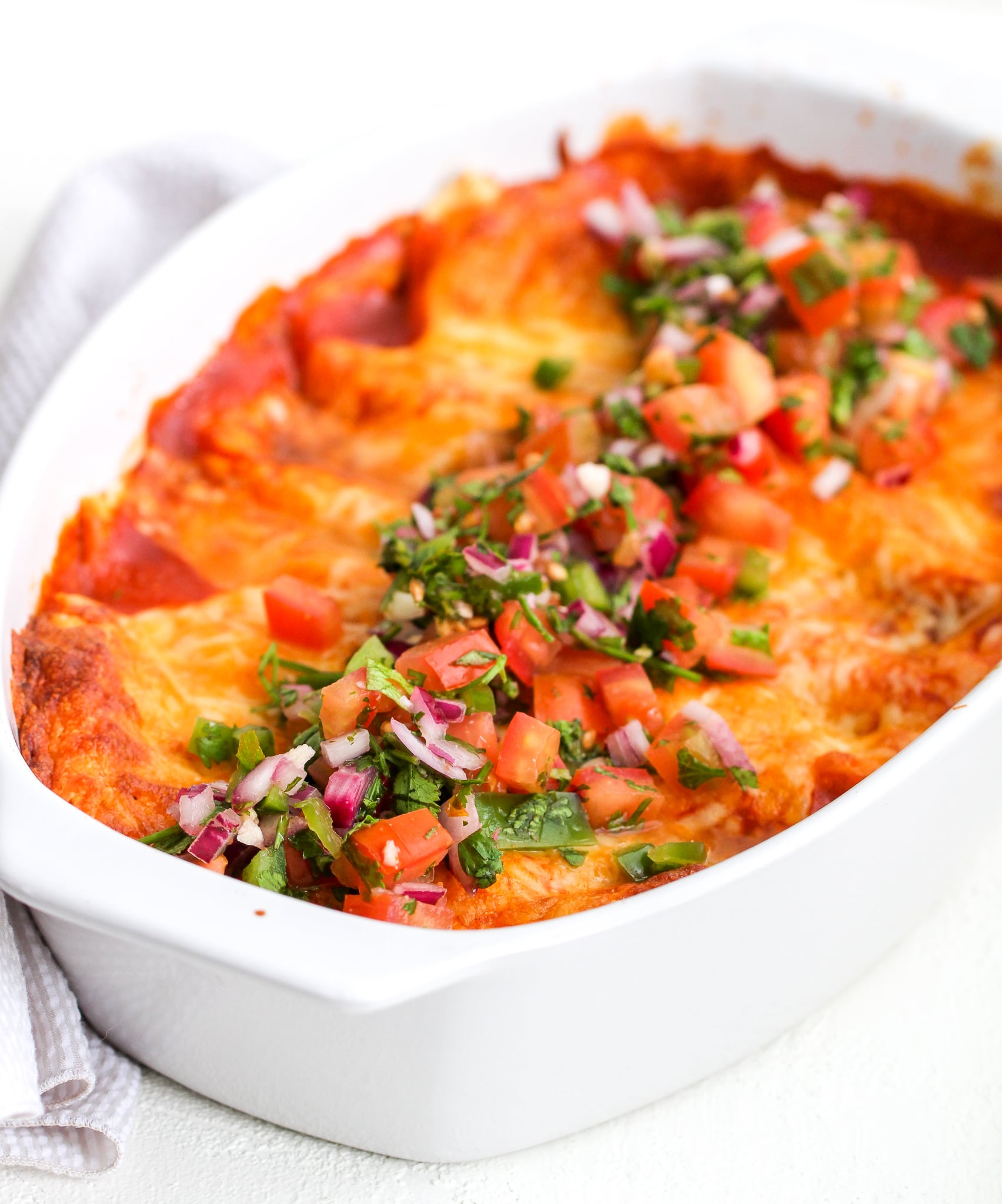 healthy enchiladas in a white baking dish topped with fresh pico de Gallo
