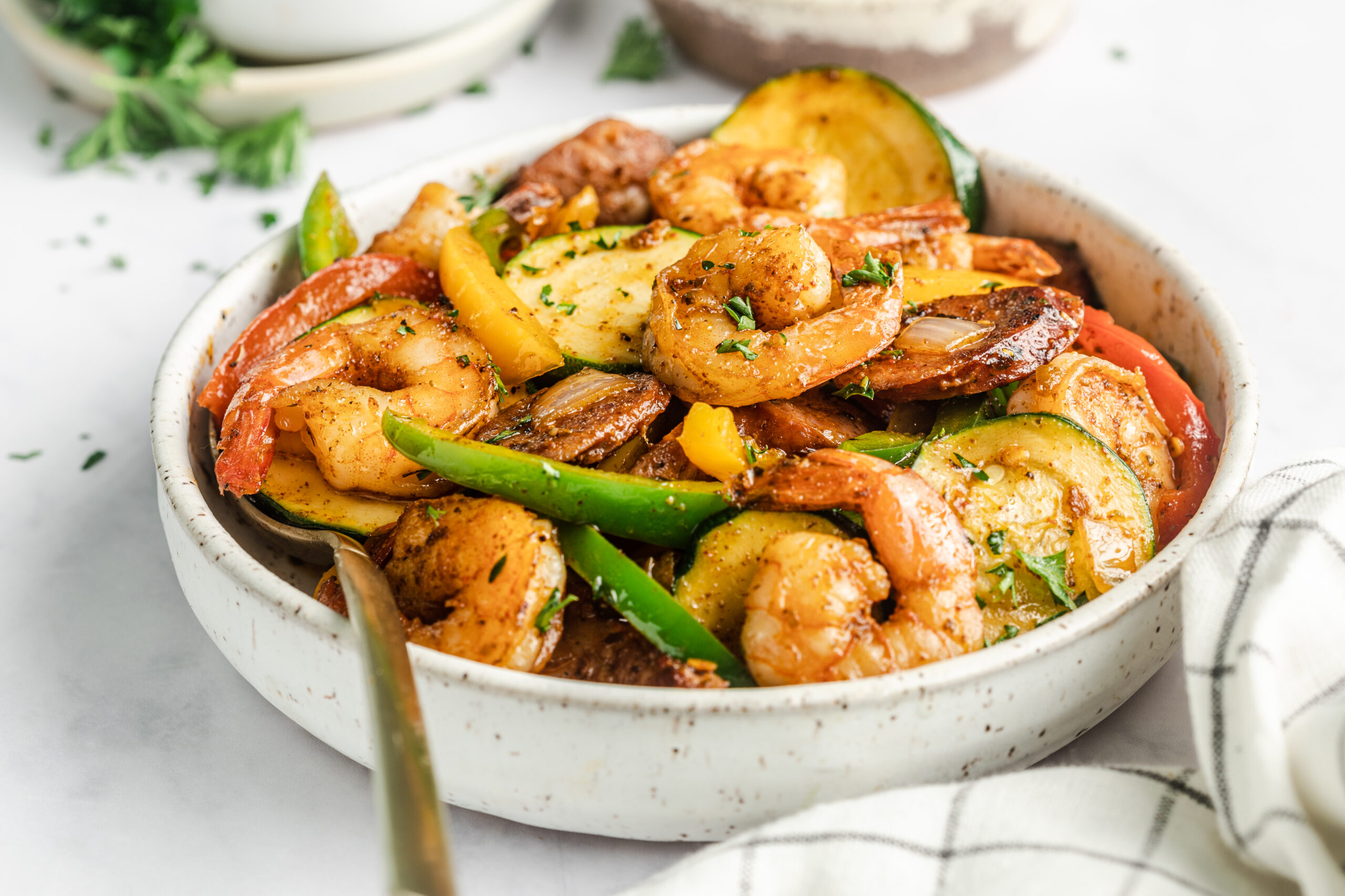shrimp and sausage skillet dish in a ceramic bowl with a gold spoon and topped with fresh parsley 