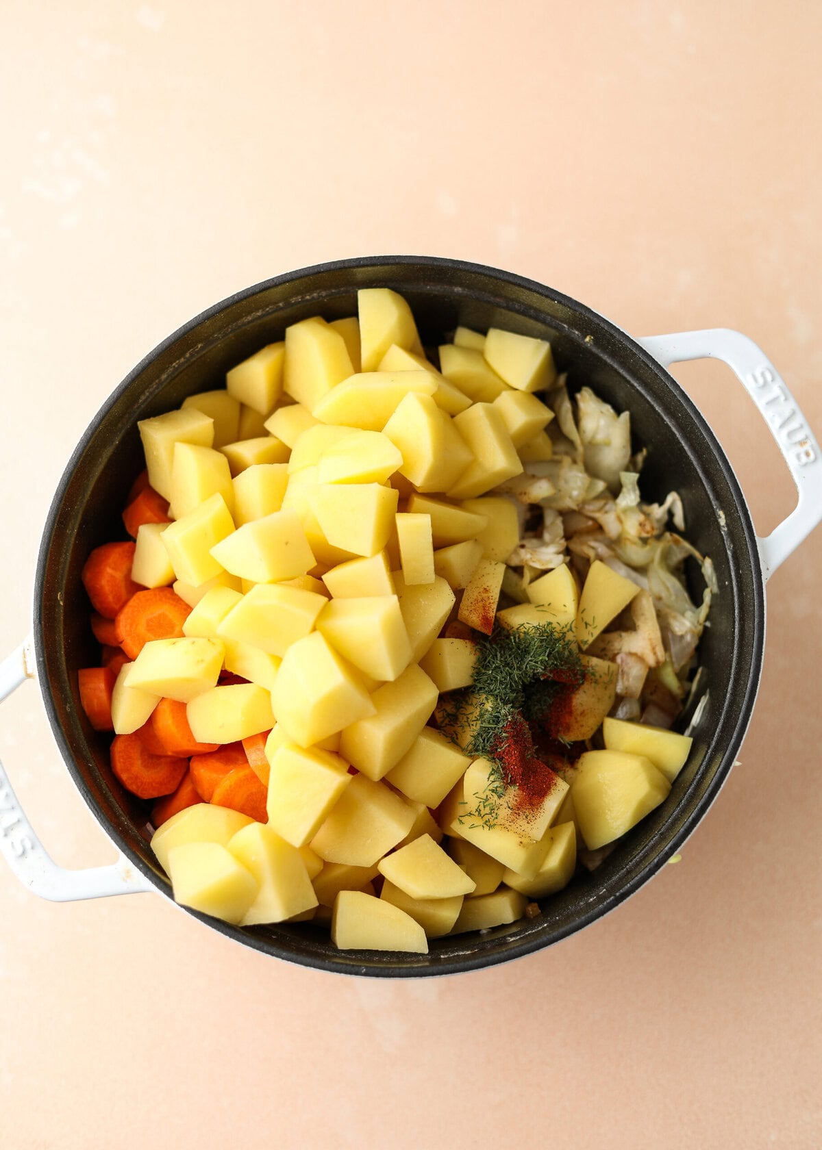 overhead shot of potatoes, carrots and spices in a dutch oven