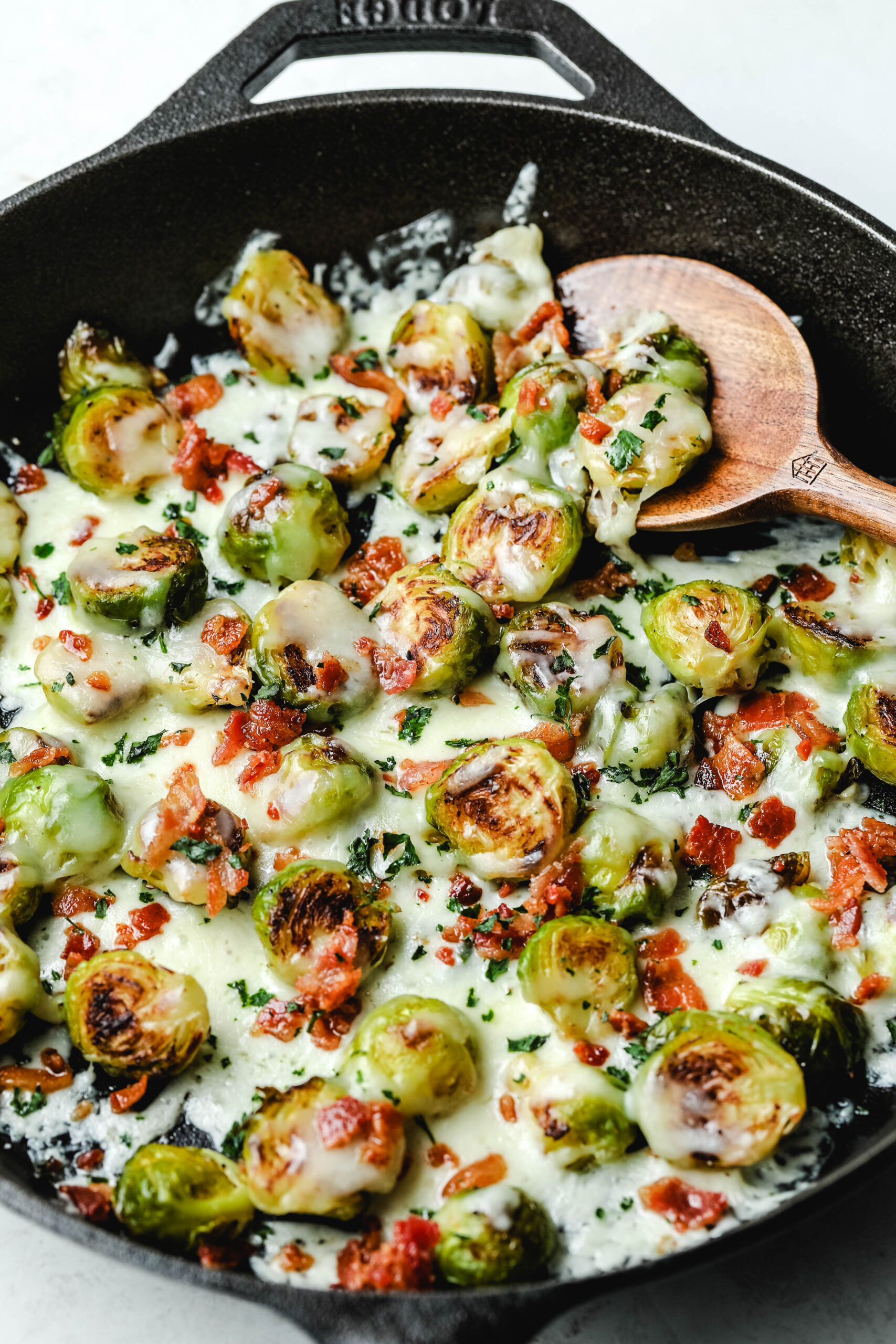 loaded brussels sprouts in a cast iron skillet topped with melted cheese, crispy bacon and fresh parsley
