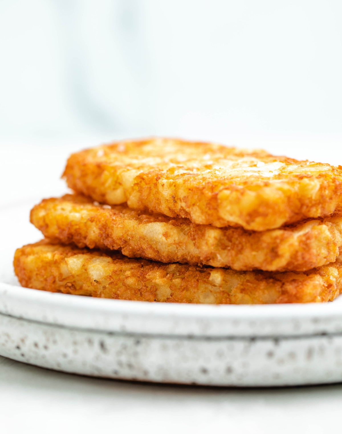 There is a stack of golden and crispy air fryer Hashbrown patties on a plate.