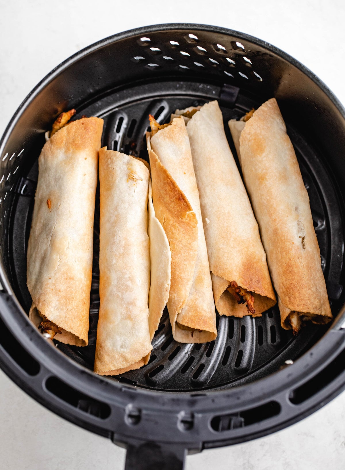 Rolled air fryer chicken taquitos lined up in the air fryer basket. 