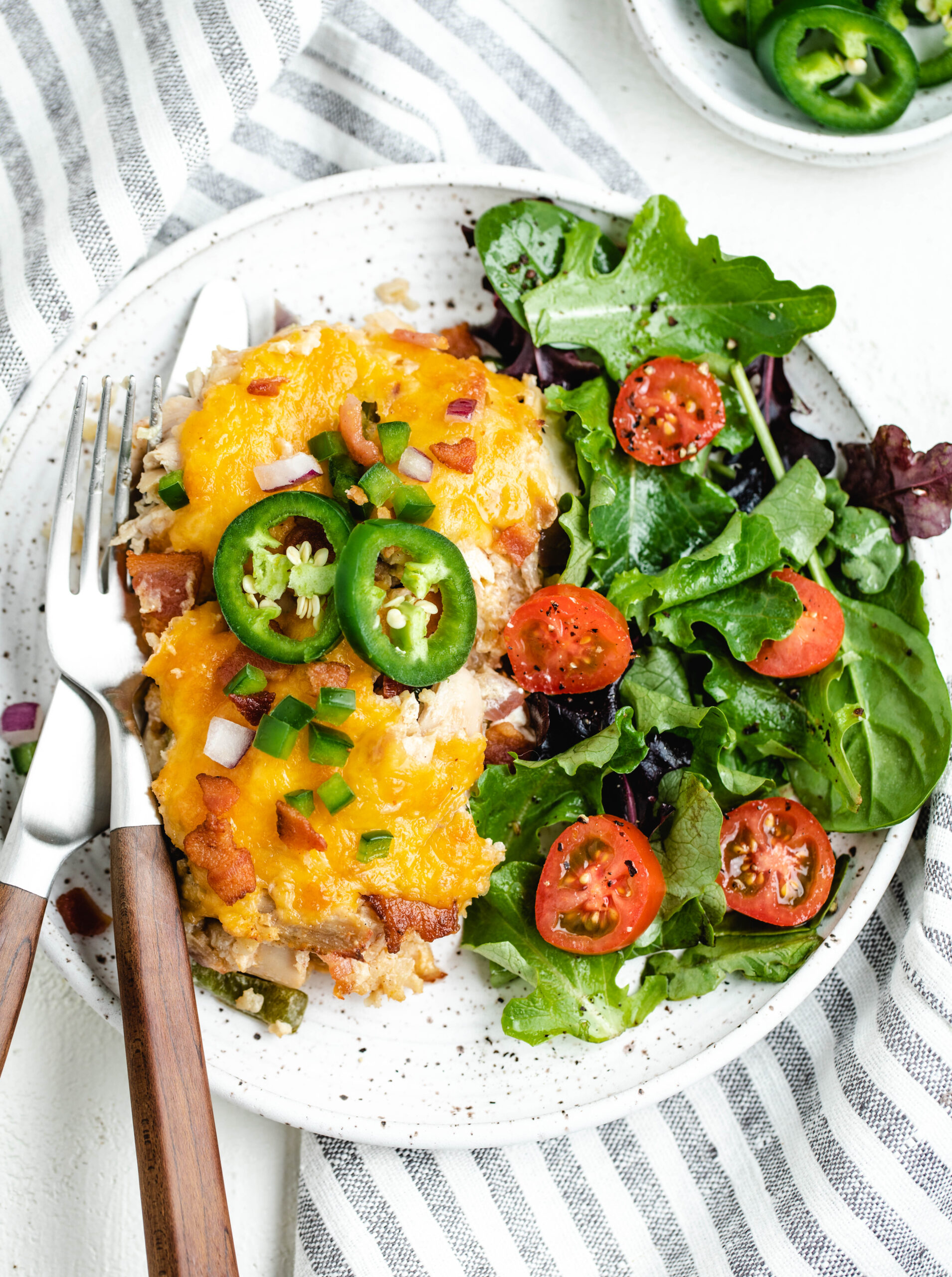 jalapeño popper casserole on a dinner plate, it is topped with fresh slice jalapeños and there is a side salad next to it. 