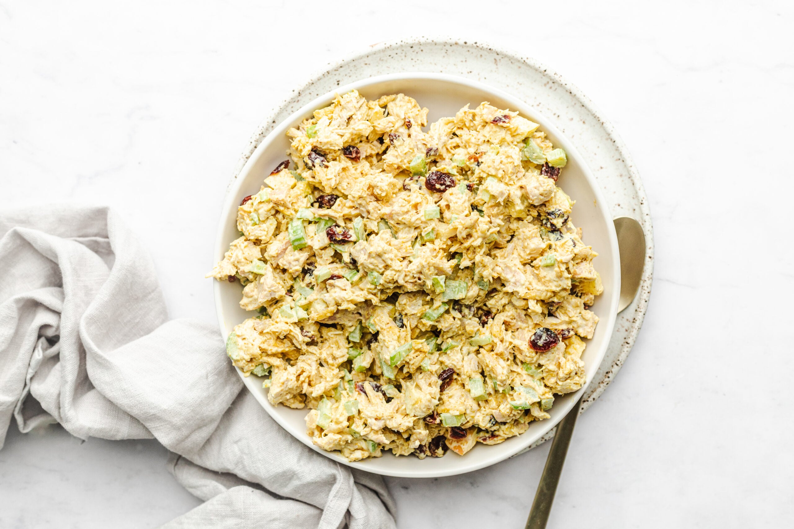 Overhead shot of curry chicken salad in a serving bowl with a cloth napkin beside it. 