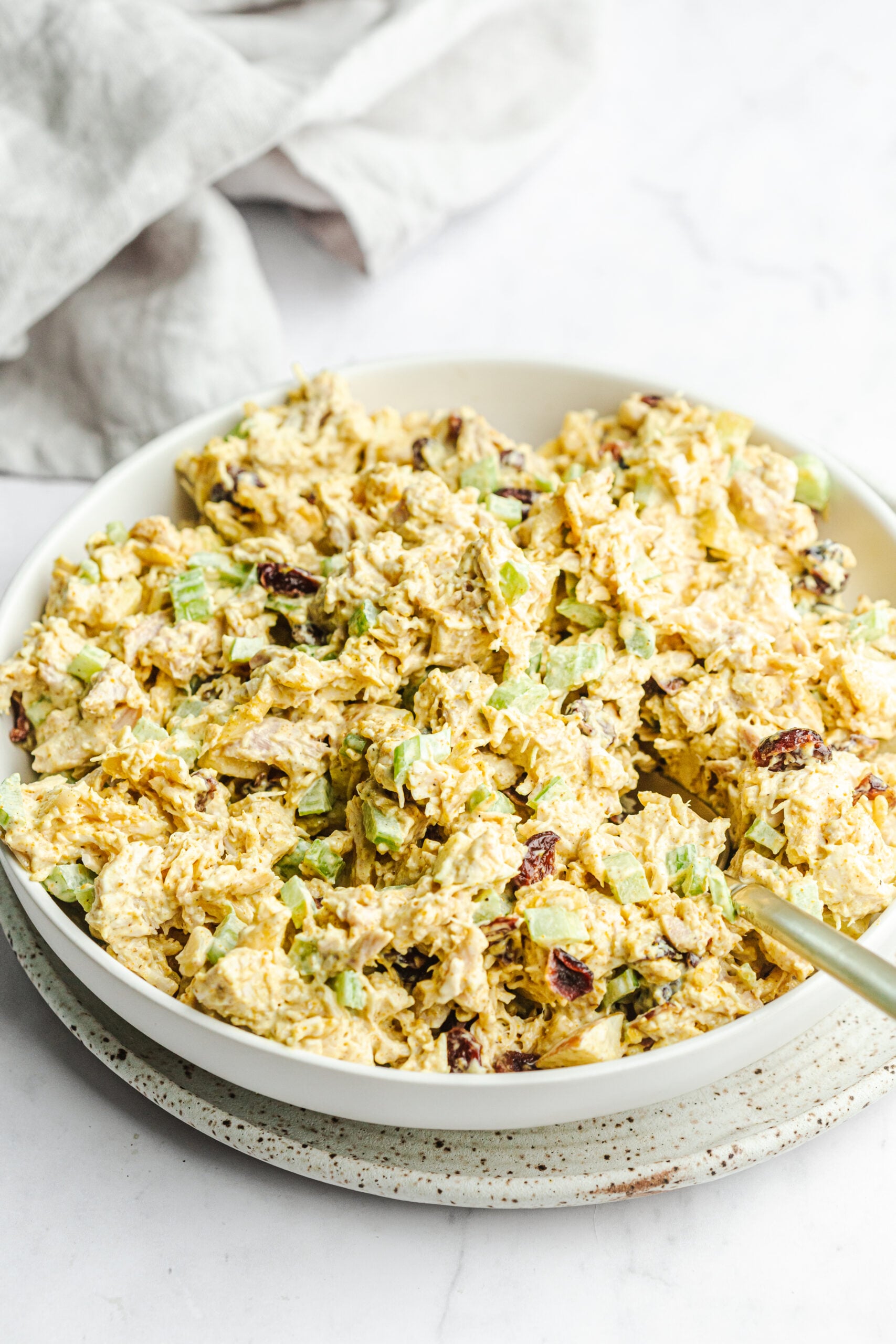 Large serving bowl filled with curry chicken salad. There is a serving spoon in the salad.