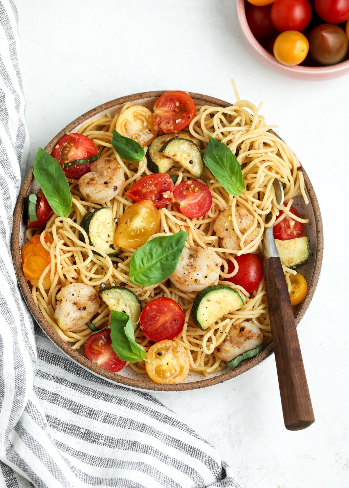 Overhead view of bowl with tomato and zucchini pasta. There is a small bowl of cherry tomatoes in the background.