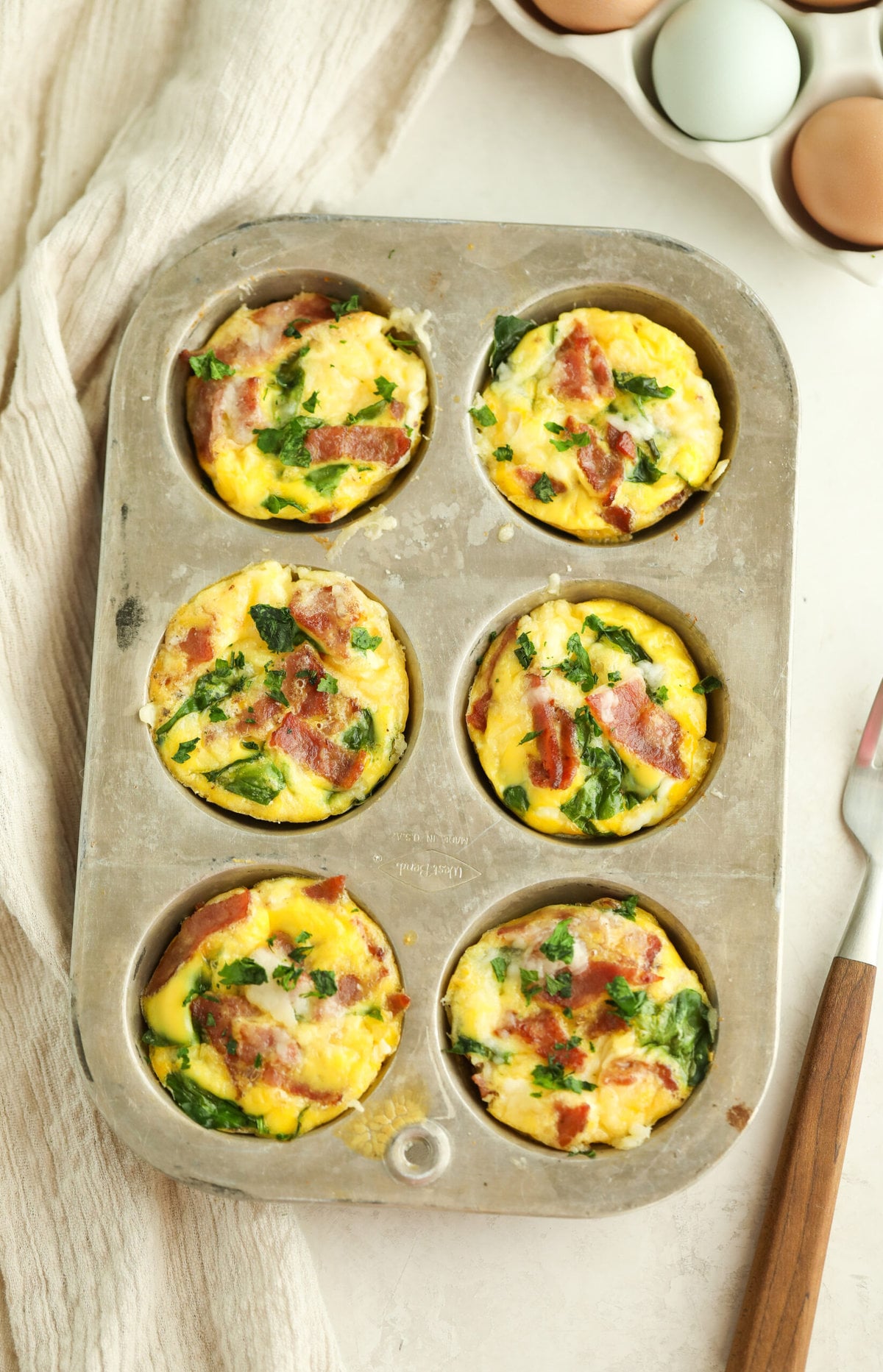 Turkey bacon egg bites in a muffin tin with a fork and linen napkin on the side 