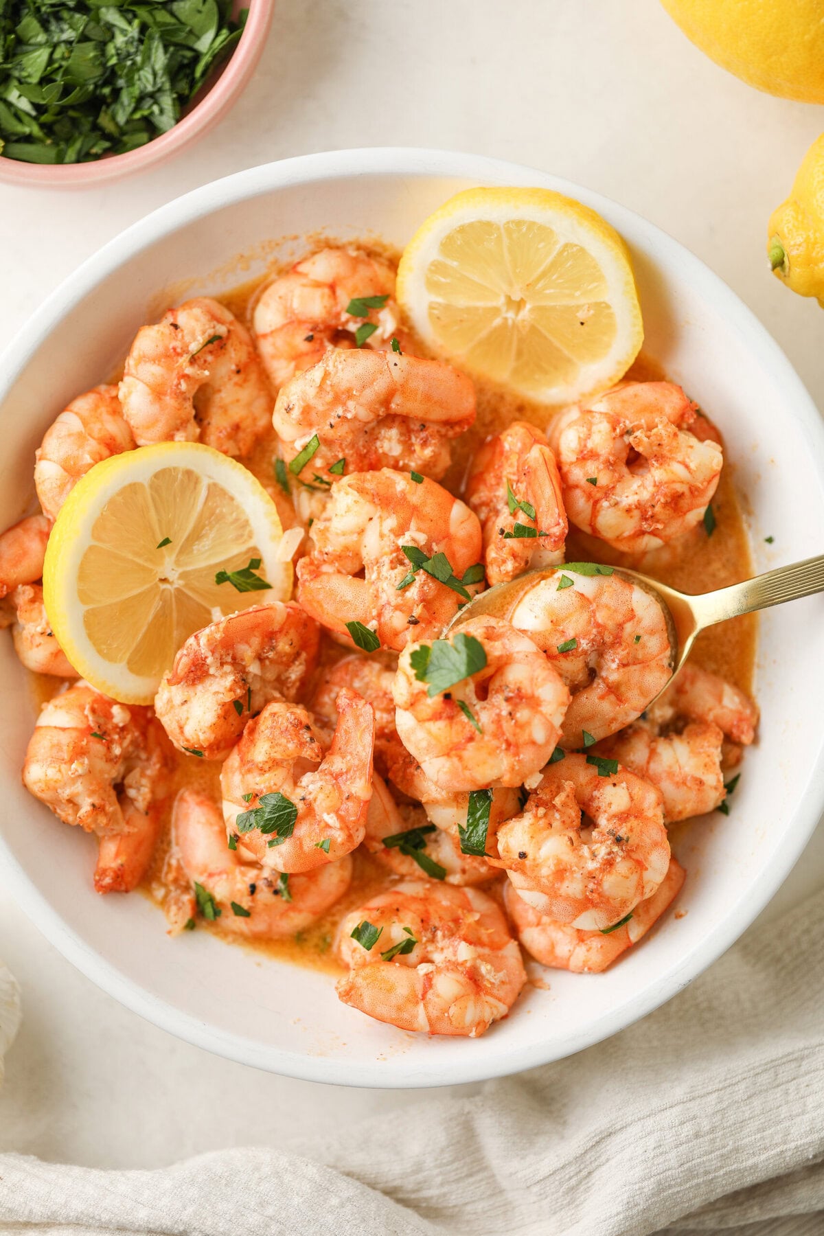Lemon garlic shrimp in a serving dish with a gold spoon in it - there are fresh lemon slices as garnish
