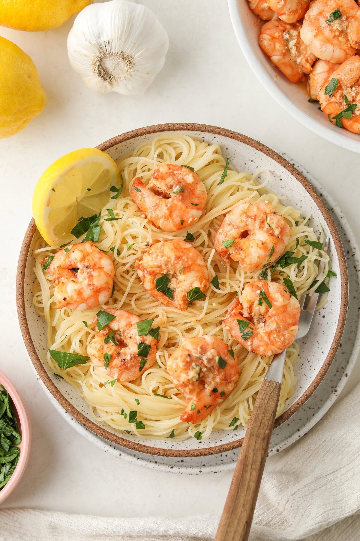 lemon garlic shrimp served over a bowl over angel hair pasta - there is fresh lemon slices and chopped parsley as garnish