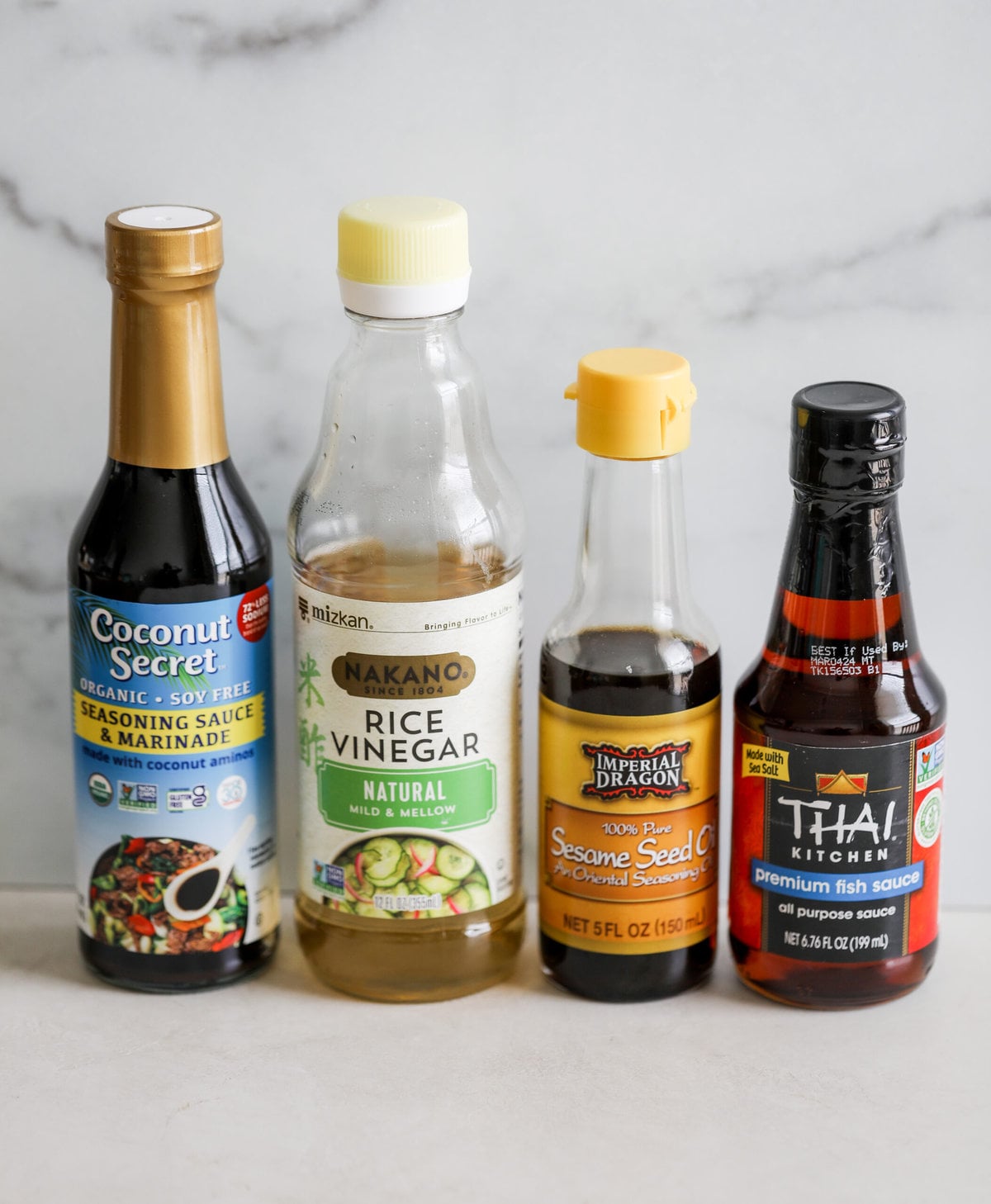 bottles of coconut aminos, rice vinegar, sesame oil and fish sauce lined up in a row