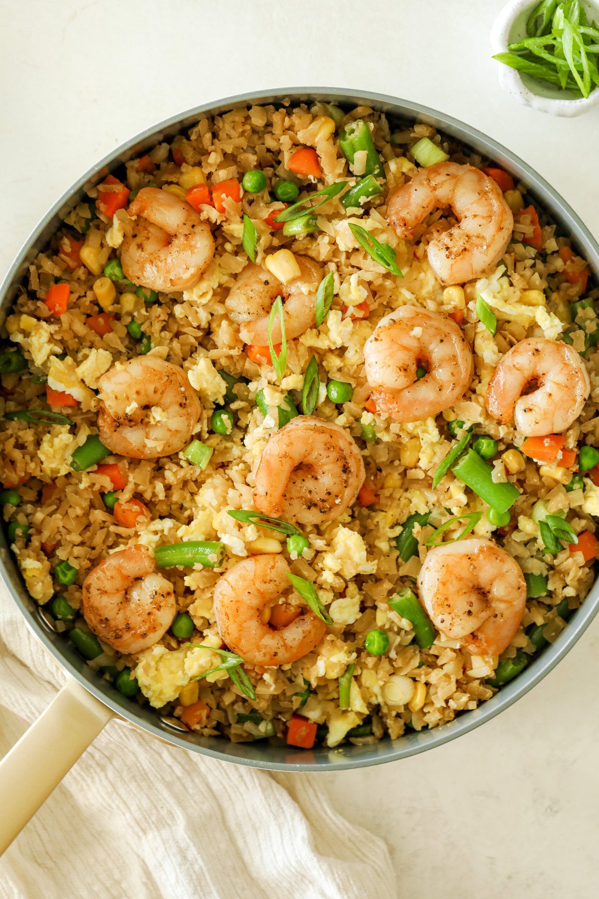 Shrimp fried cauliflower rice in a large white skillet. It is topped with fresh sliced green onions.