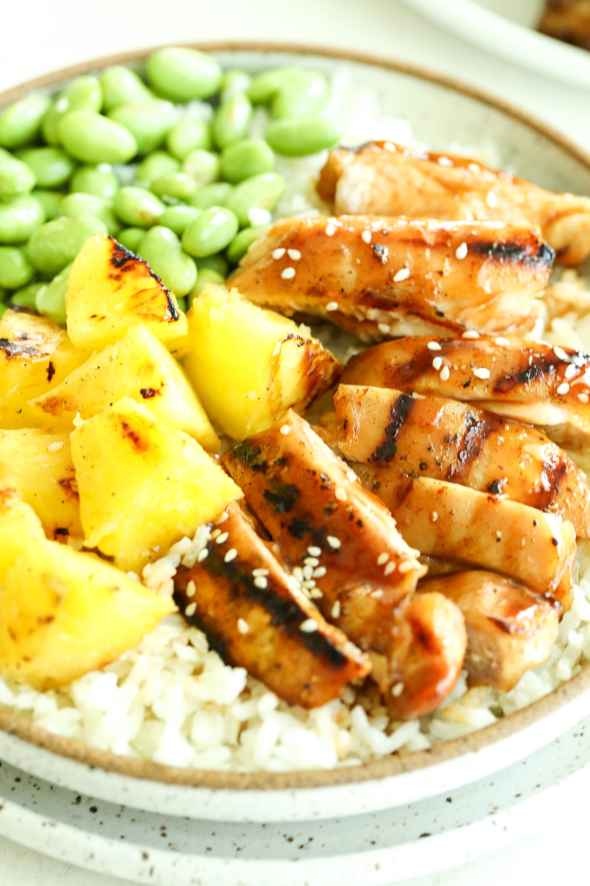Grilled teriyaki chicken and pineapple over a bed of rice. There is edamame on the side and sesame seeds on top.