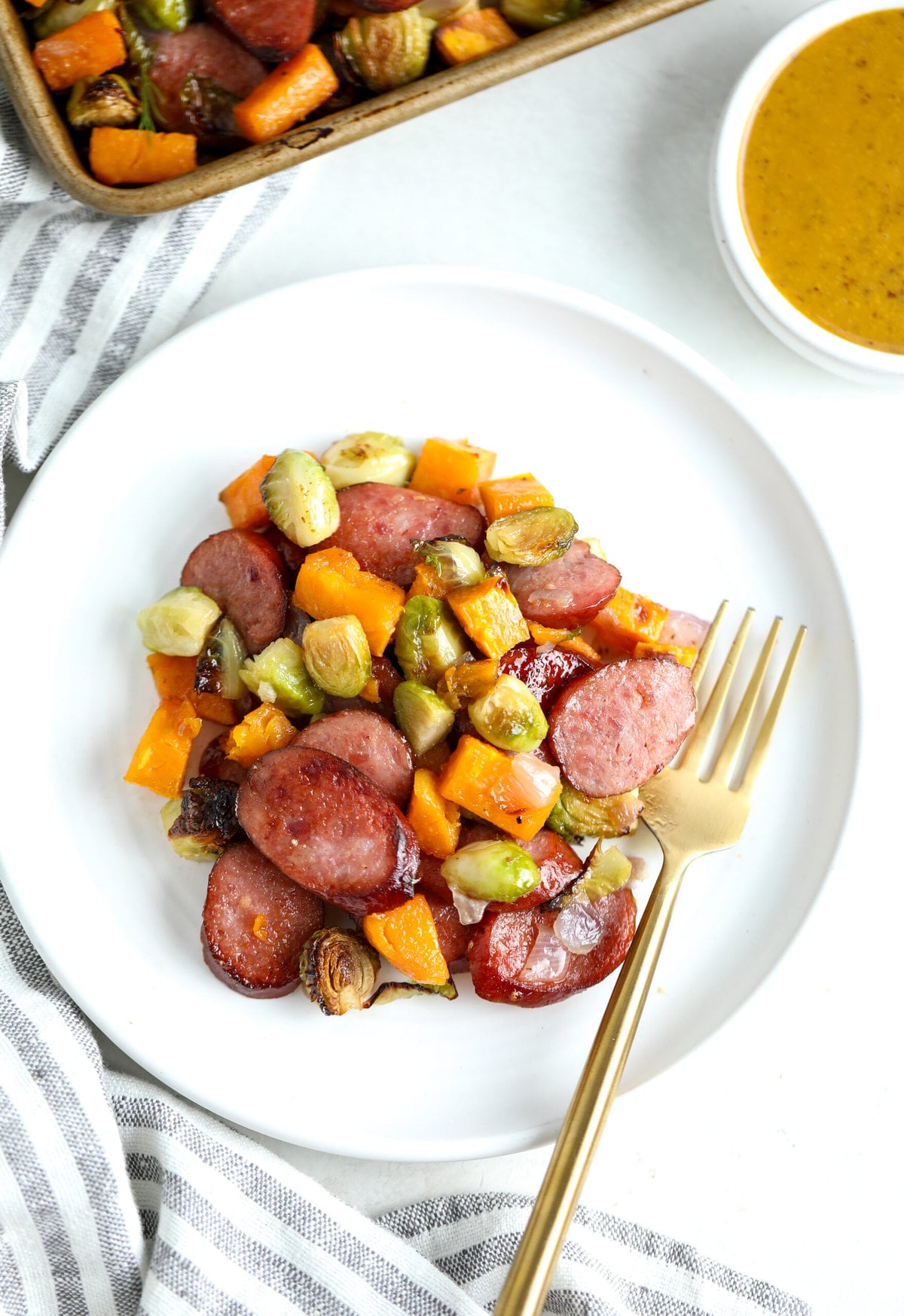 Sausage and veggies on a white dinner plate with a side condiment of maple mustard sauce.