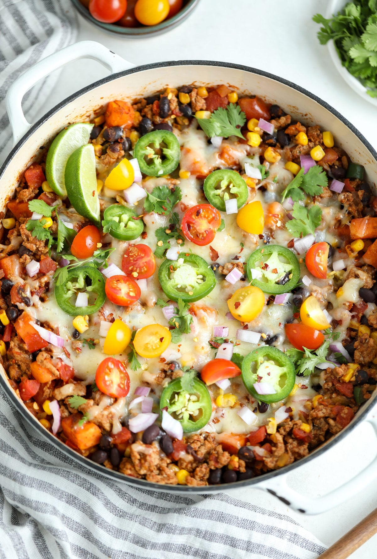healthy turkey taco skillet dinner shown in a large white ceramic skillet. It is topped with fresh tomatoes, jalapeños and cilantro. 