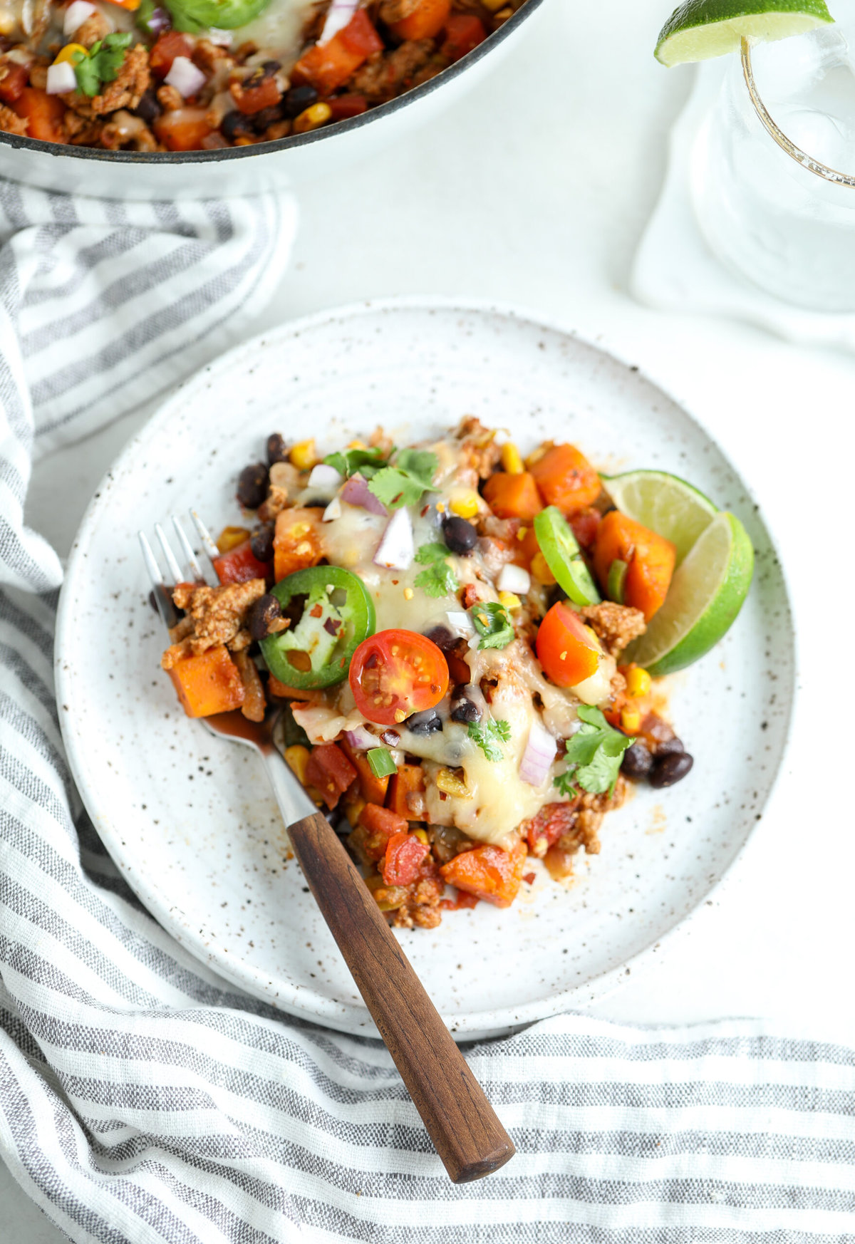 Serving of turkey taco skillet on a speckled ceramic plate with a fork beside it. There is a glass of water on the side.