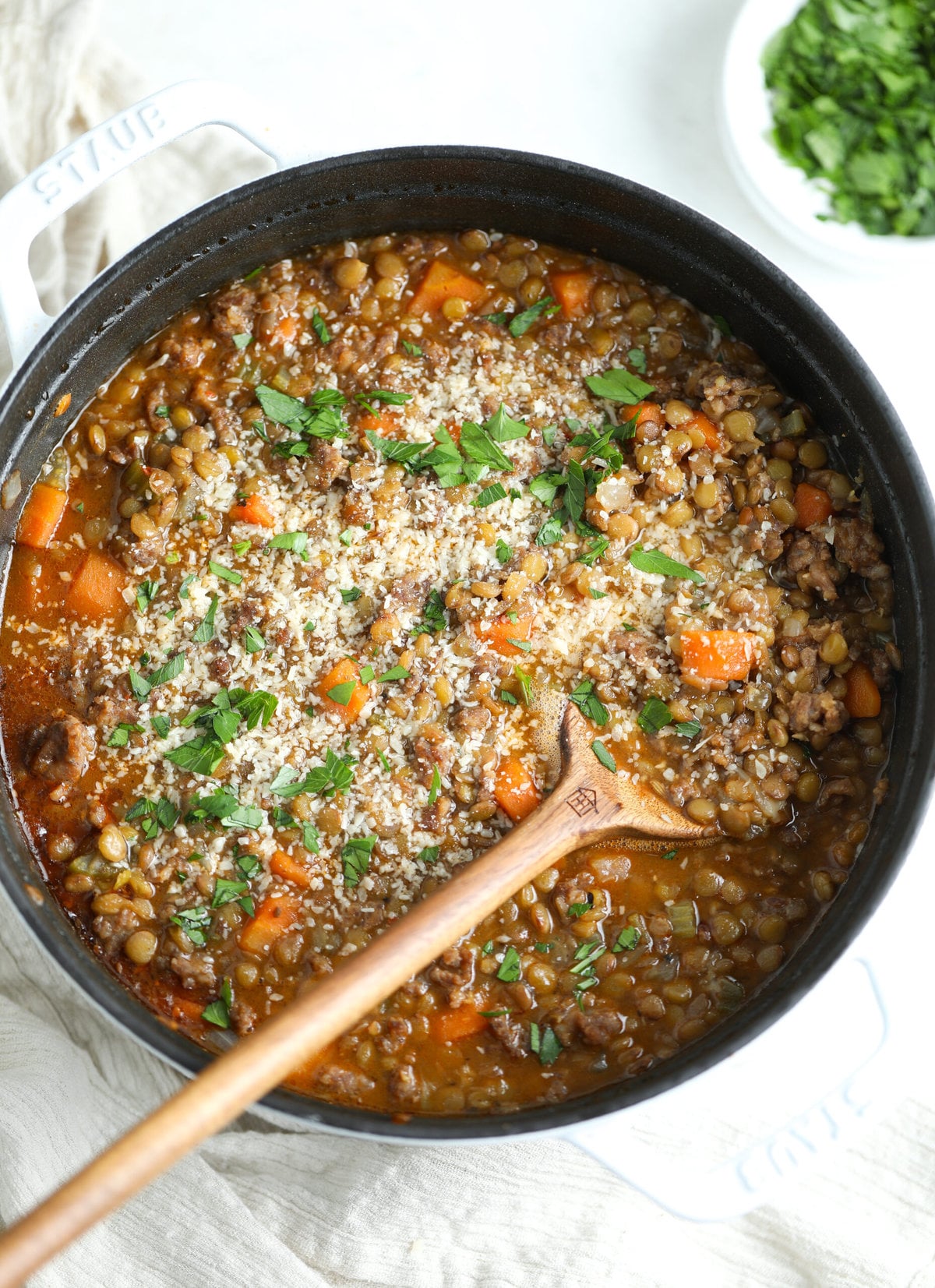 Sausage and lentil soup in a large dutch oven pan. It is topped with fresh grated parmesan and fresh chopped parsley. 