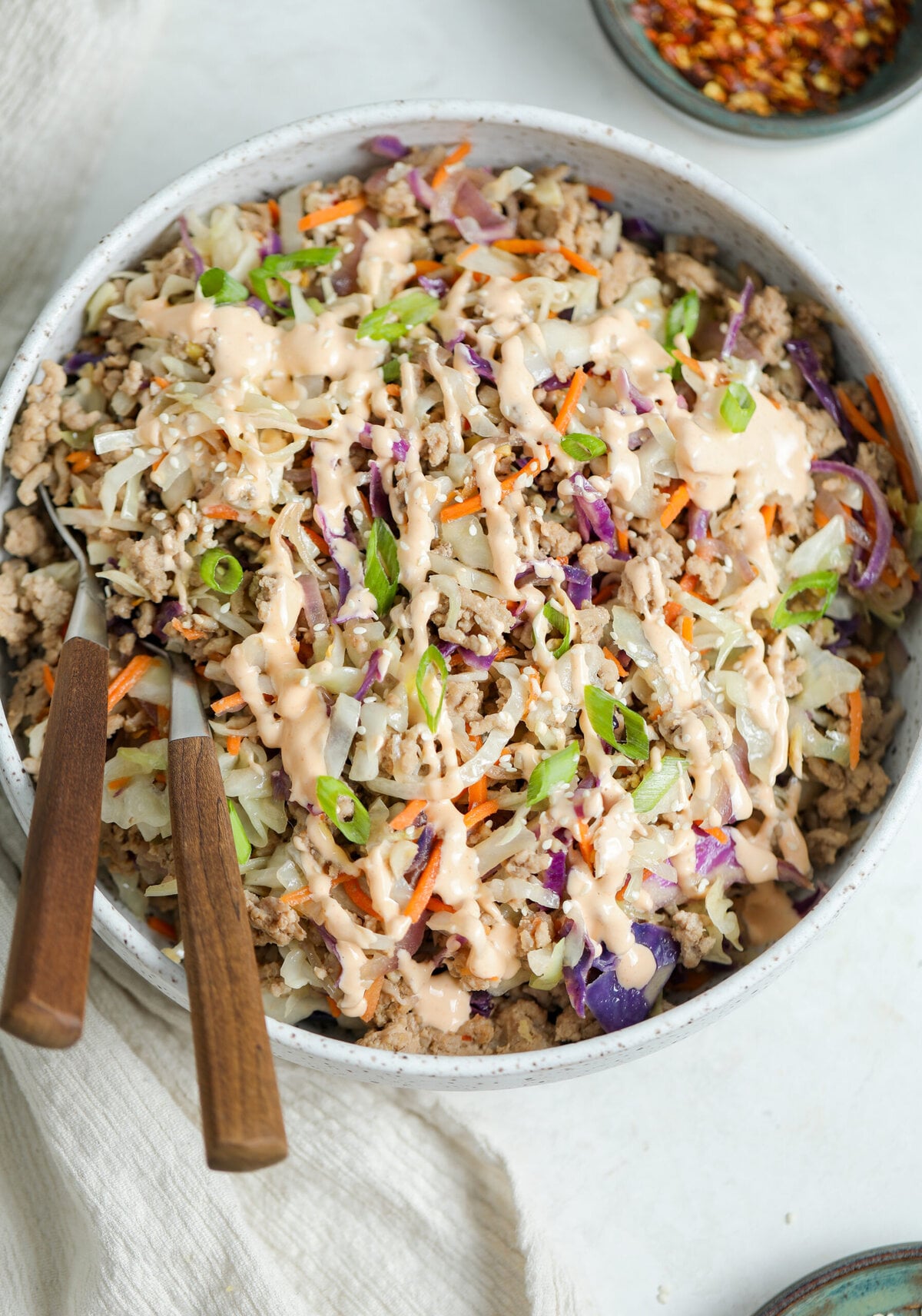 Egg roll in a bowl served in a large ceramic dish with sauce drizzled over the top.