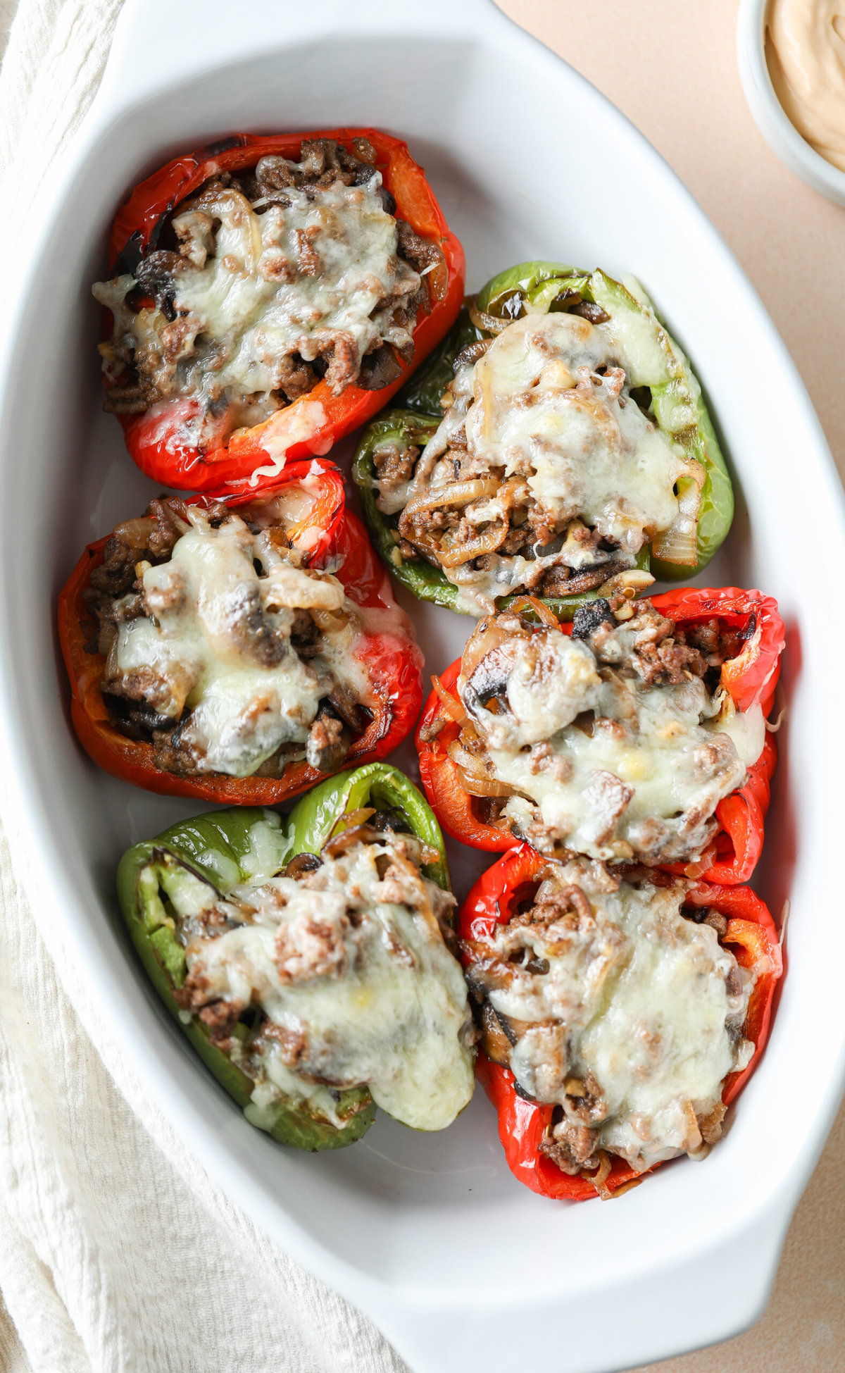 Philly cheesesteak stuffed peppers in a white baking dish. There is melted cheese on the top.