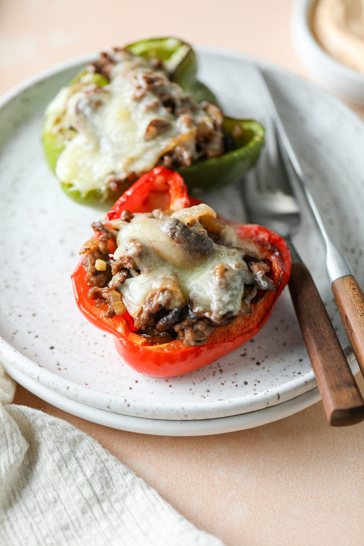 Two low carb Philly cheesesteak stuffed peppers on a plate with a fork and knife beside it.