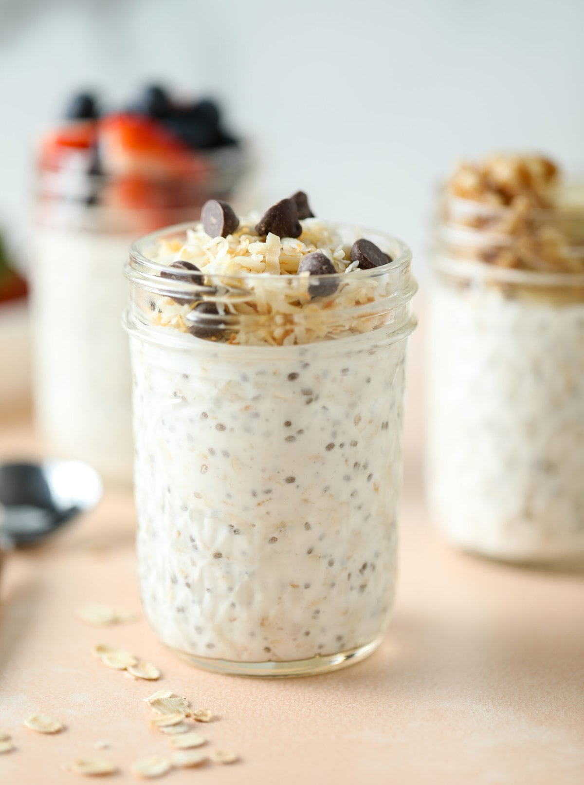 3 jars of overnight oats with various toppings - the focus is on a jar with toasted coconut and chocolate chips on top of the oats