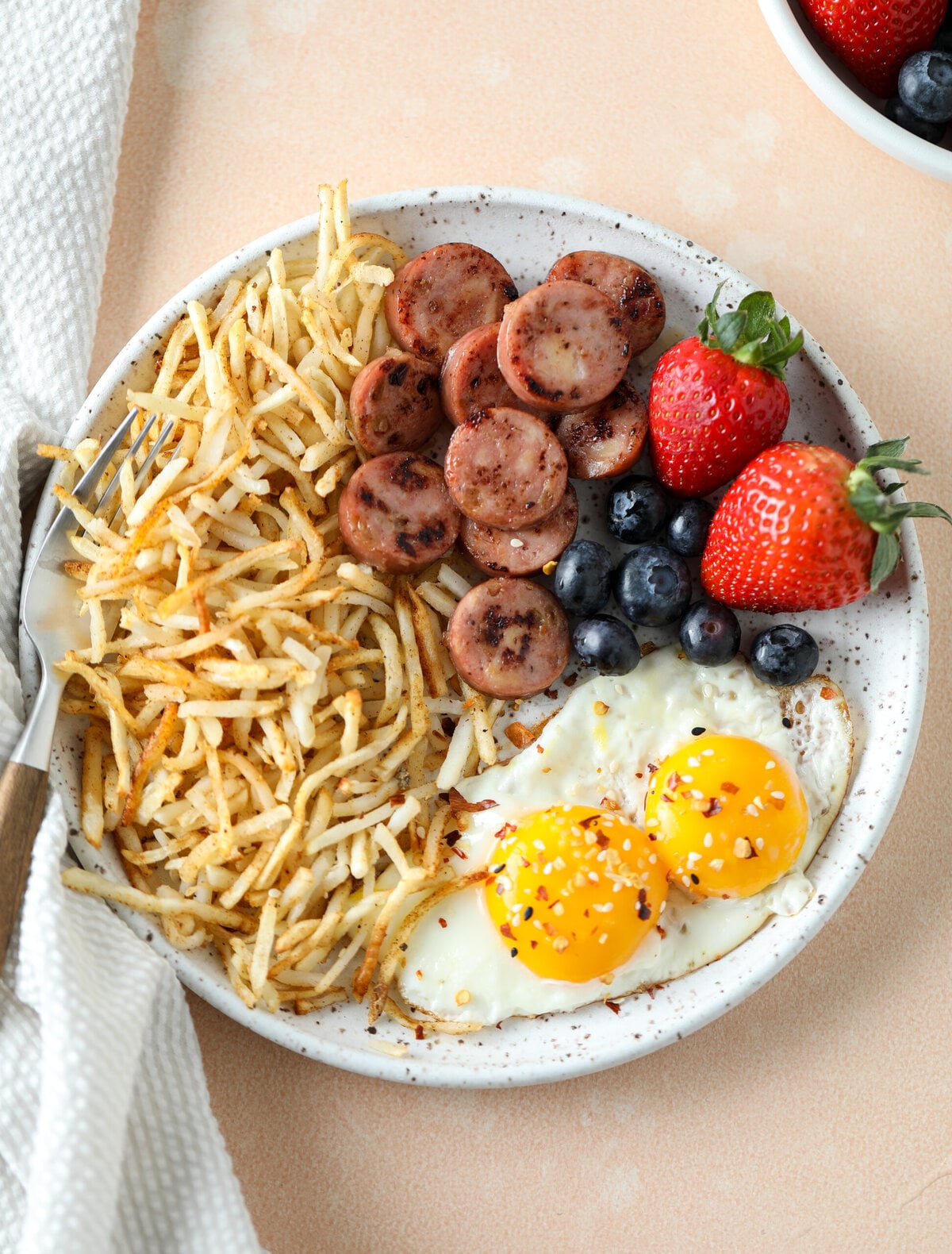 air fryer shredded hash browns on a plate with eggs, sausage and fresh berries