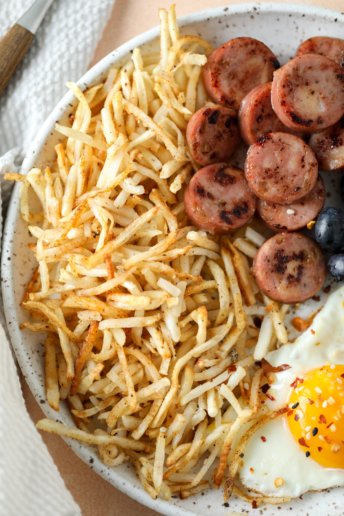 close up of air fryer shredded hash browns on a breakfast plate with eggs, sausage and fresh fruit